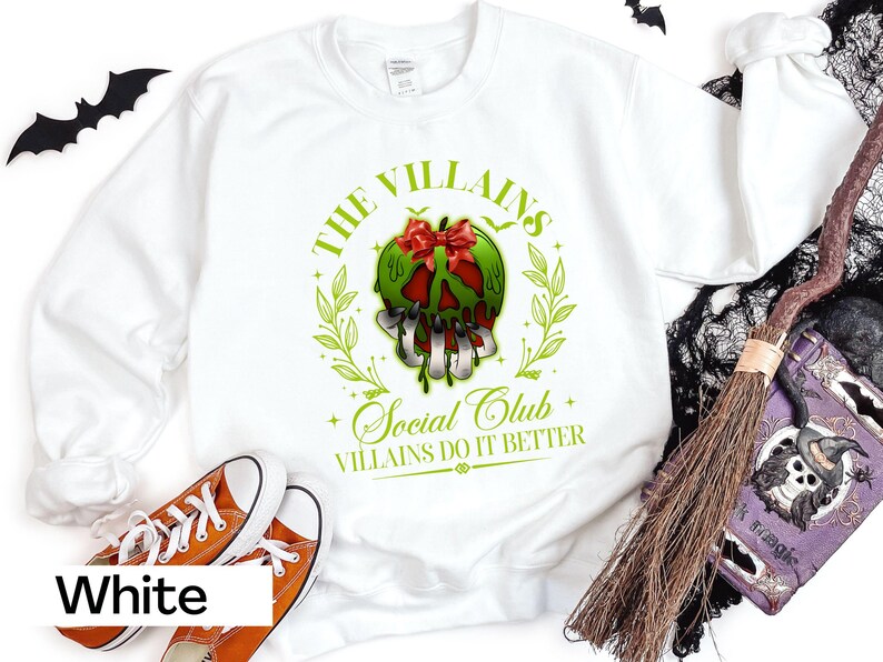 May include: White sweatshirt with a graphic featuring a green apple-shaped skull with a red bow, surrounded by green leaves. The text reads "The Villains Social Club, Villains Do It Better". Orange sneakers are at the bottom.
