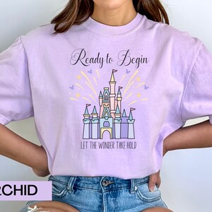 May include: A lavender t-shirt with a graphic of Cinderella's castle and the text "Ready to Begin" and "Let the Wonder Take Hold".