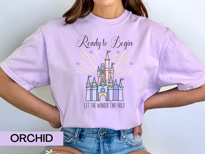 May include: A lavender t-shirt with a graphic of Cinderella's castle and the text "Ready to Begin" and "Let the Wonder Take Hold".
