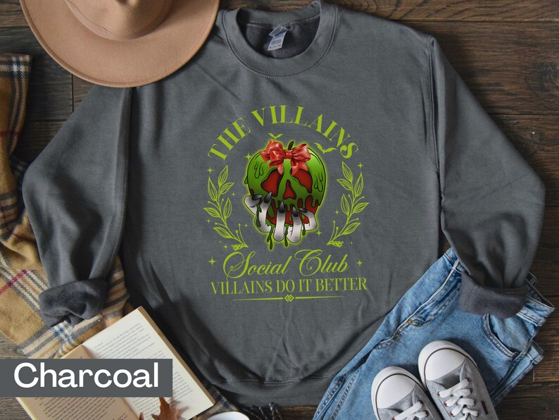 May include: Charcoal gray sweatshirt featuring a graphic of a green apple with a red bow, dripping with poison, and the text "The Villains Social Club Villains Do It Better". The design is surrounded by a green wreath.