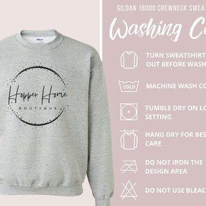 May include: A light gray Gildan 18000 crewneck sweatshirt with the text "Hopper Home Boutique" in a black circular design. Washing instructions are displayed on the right side of the image.