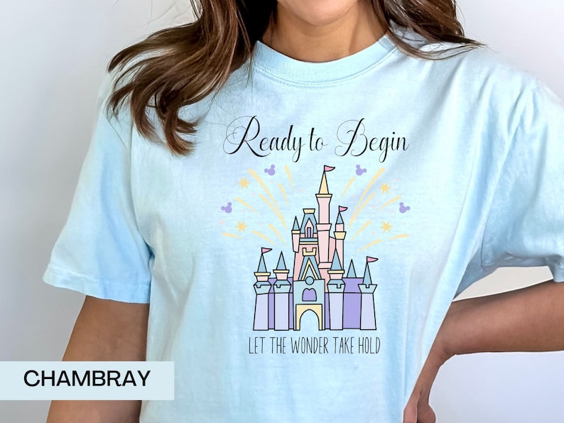 May include: A light blue t-shirt with a graphic of Cinderella's castle and fireworks. The text "Ready to Begin" and "Let the Wonder Take Hold" are printed on the shirt. Chambray.