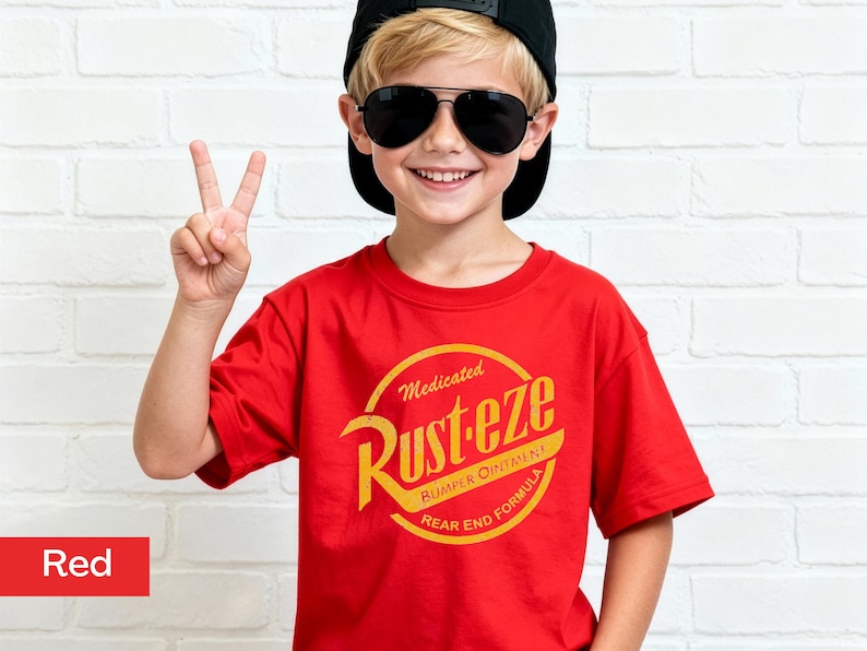 May include: A red t-shirt with a yellow and orange graphic that says "Rust-eze" in a circular design. The shirt is worn by a person wearing a black cap and sunglasses, making a peace sign.