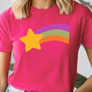 May include: A magenta t-shirt featuring a yellow star and a rainbow design in purple, green, and orange. The short-sleeved shirt is made of a soft material.