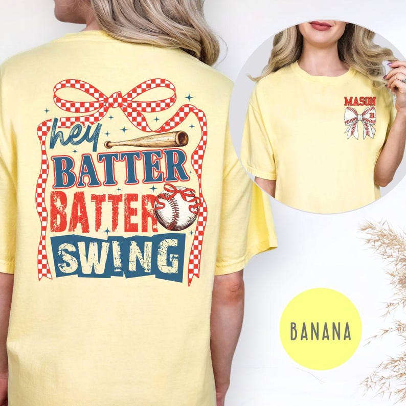 May include: A light yellow t-shirt with baseball-themed graphics. The back features the text "Hey Batter Batter Swing" with a baseball bat and ball design. The front has a smaller baseball bow design with the name "MASON" above it.