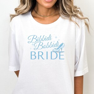 May include: White t-shirt with blue text that says "Bibbidi Bobbidi Bride" and a blue glass slipper graphic.
