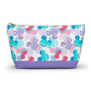 May include: A white zippered pouch with a purple bottom. The pouch has a repeating pattern of colorful geometric Mickey Mouse heads.
