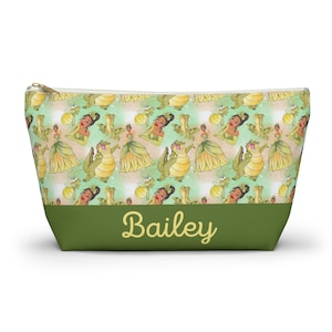 May include: A green and beige zippered makeup bag with a repeating pattern of a cartoon princess and a green alligator. The bag has a green bottom with the name "Bailey" written in yellow letters.