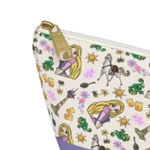 May include: A white zippered pouch with a repeating pattern of Rapunzel, Pascal the chameleon, a horse, a frying pan, a tower, and a sun. The zipper pull is gold.