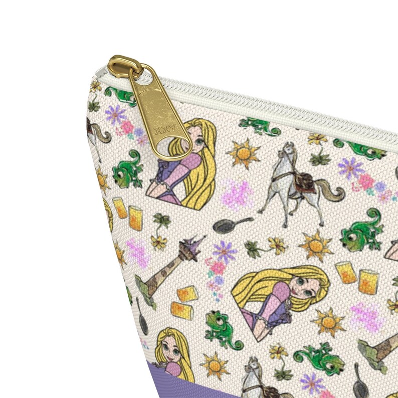 May include: A white zippered pouch with a repeating pattern of Rapunzel, Pascal the chameleon, a horse, a frying pan, a tower, and a sun. The zipper pull is gold.