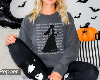May include: A dark gray sweatshirt with a silhouette of a bride and the text "Who's afraid of little old me?" repeated multiple times. The text is in white.