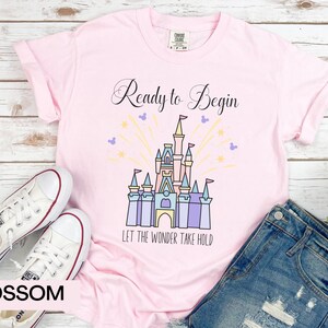 May include: Pink t-shirt with a black graphic of Cinderella's castle with fireworks and the text "Ready to Begin" and "Let the Wonder Take Hold".