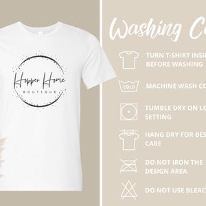 Pu&ograve; includere: T-shirt bianco con girocollo e maniche corte. La maglietta presenta un logo circolare nero con la scritta "Hopper Home Boutique". Le istruzioni per il lavaggio sono visualizzate sul lato destro della maglietta.