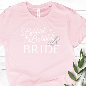 May include: Pink t-shirt with the text "Bibbidi Bobbidi Bride" in white with a glass slipper graphic.