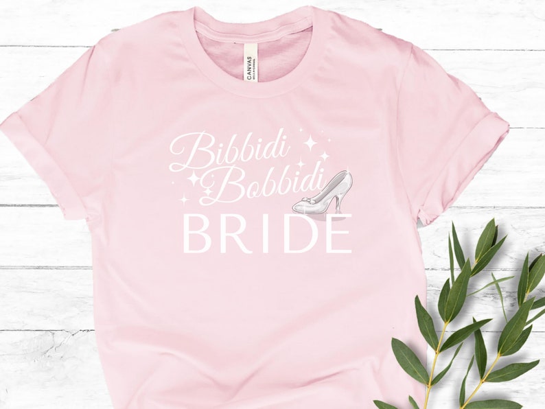 May include: Pink t-shirt with the text "Bibbidi Bobbidi Bride" in white with a glass slipper graphic.