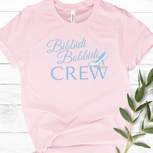 May include: Pink t-shirt with the text "Bibbidi Bobbidi Crew" in blue lettering and a blue glass slipper graphic.