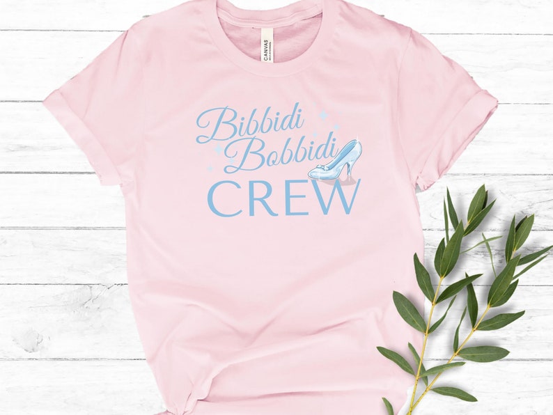 May include: Pink t-shirt with the text "Bibbidi Bobbidi Crew" in blue lettering and a blue glass slipper graphic.