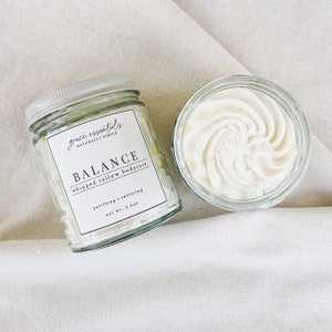 May include: A glass jar of whipped tallow bodycare labeled "grace essentials NATURALLY SIMPLE BALANCE whipped tallow bodycare purifying + restoring net wt. 3.5oz".