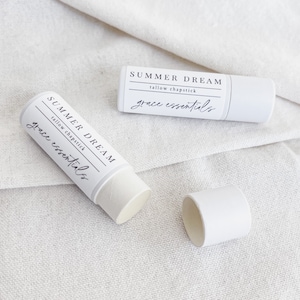 May include: Two white tubes of lip balm with the label "SUMMER DREAM tallow chapstick grace essentials" on a white fabric background.
