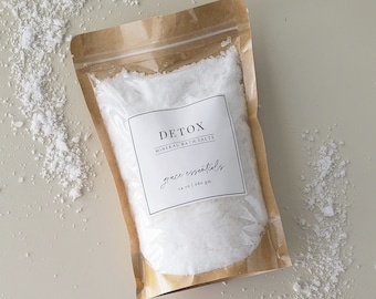 May include: A brown paper pouch filled with white mineral bath salts. The pouch has a white label with the text "DETOX MINERAL BATH SALTS grace essentials 14 oz | 680 gm".