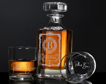 May include: A crystal decanter with a stopper and two matching glasses. The decanter is engraved with a monogram and the name "Robert Brown".