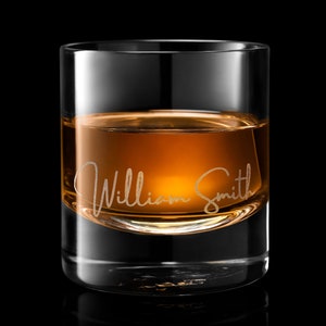May include: A clear glass rocks glass with a gold rim filled with amber colored liquid. The glass is engraved with the name "William Smith".