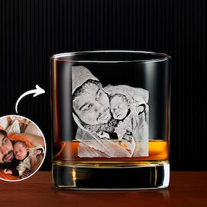 May include: A clear whiskey glass with a laser-etched image of a father holding a baby. The glass is filled with amber liquid. A smaller inset image shows the original photo.