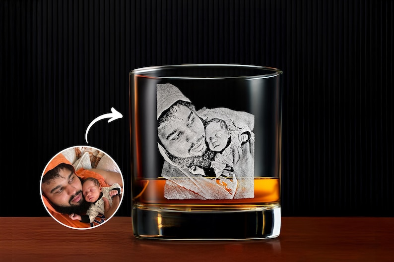 May include: A clear whiskey glass with a laser-etched image of a father holding a baby. The glass is filled with amber liquid. A smaller inset image shows the original photo.