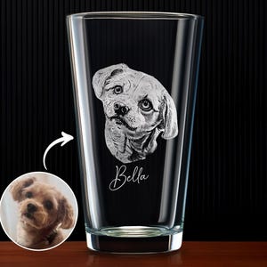 May include: A clear glass pint glass with a detailed etched portrait of a dog's face. The dog's name, "Bella," is written in cursive below the portrait. A small circular image of the dog is next to the glass.