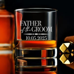 以下が含まれることがあります： 前面に「Father of the Groom」というテキストと「10.05.2025」という日付がエッチングされた透明なガラス製のロックグラスです。
