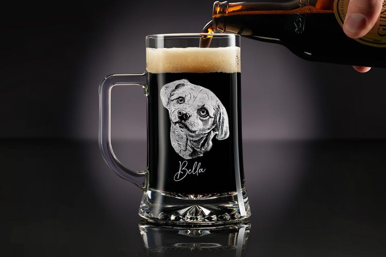 May include: A clear glass beer mug with a handle, filled with dark beer and foam. The mug features an etched image of a dog's face and the name "Bella" in cursive. Beer is being poured from a bottle.