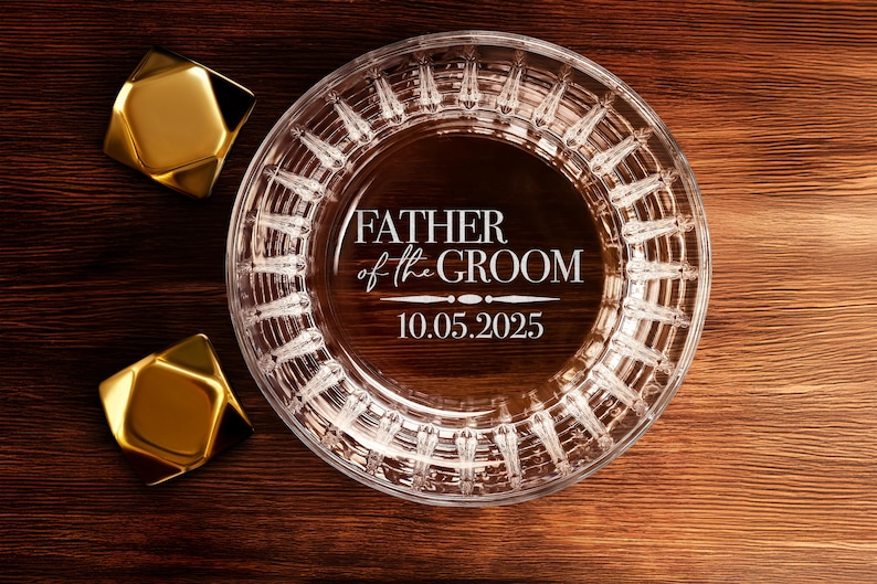 以下が含まれることがあります： 装飾的なパターンと「Father of the Groom」の刻印、および「10.05.2025」の日付が刻まれた透明なガラス製の灰皿です。