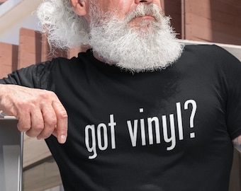 May include: A man wearing a black t-shirt with the text "got vinyl?" printed in white. He is wearing sunglasses and has a long white beard.