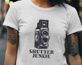 May include: White t-shirt with a black and white illustration of a vintage camera and the text "Shutter Junkie".