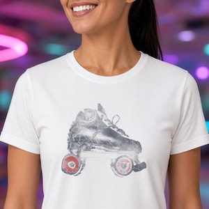 May include: A white short-sleeved t-shirt featuring a graphic print of a roller skate. The skate is rendered in a distressed gray texture with two prominent red wheels visible at the base, showcasing a classic quad skate design.