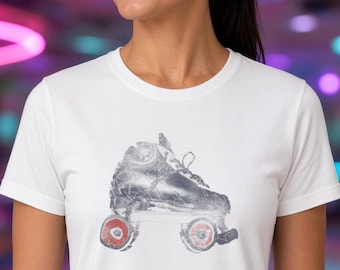 May include: A white short-sleeved t-shirt featuring a graphic print of a roller skate. The skate is rendered in a distressed gray texture with two prominent red wheels visible at the base, showcasing a classic quad skate design.