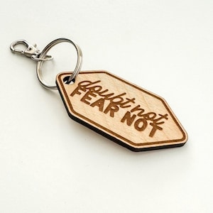 May include: Wooden keyring with a hexagonal shape and a silver key ring. The keyring has the words "doubt not FEAR NOT" engraved on it.