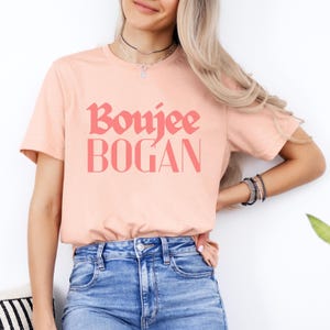 May include: A pink t-shirt with the text "Boujee Bogan" printed in a bold, pink font.
