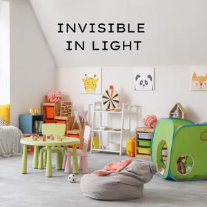 May include: A child's playroom with a green table and chairs, a gray beanbag chair, and a green and blue play tent. The room also features artwork of animals and the text "INVISIBLE IN LIGHT".