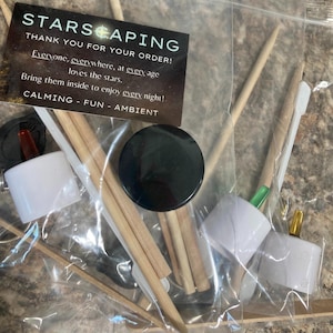 May include: A clear plastic bag containing various items. A black circular object, wooden sticks, and white plastic components are visible. A card with the text "STARSCAPING" and other text is also included.