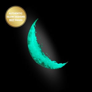 May include: A glowing, turquoise crescent moon shape against a black background. The image includes a gold circle with the text "AUTHENTIC GLOW DESIGNS NOT DECALS". The moon has a textured, illuminated appearance.
