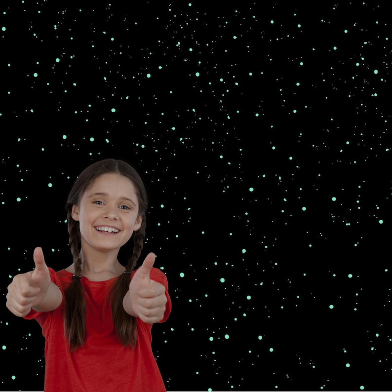 May include: A young person with brown hair in pigtails wearing a red shirt gives a thumbs-up gesture with both hands. The background is black with small, scattered, light-green dots, resembling stars.