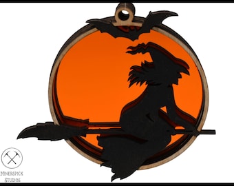 Op de afbeelding: Een houten Halloween-versiering met een zwart silhouet van een heks die op een bezem vliegt voor een oranje maan. De versiering heeft een vleermuisontwerp aan de bovenkant.