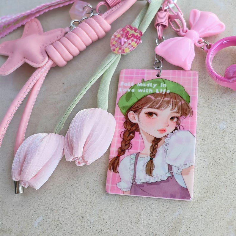 May include: A collection of pink accessories, including a star-shaped charm, a bow, and a rectangular tag with a cartoon girl illustration. The tag reads "Fall Madly in Love with Life". Also included are two pink tulip-shaped charms.