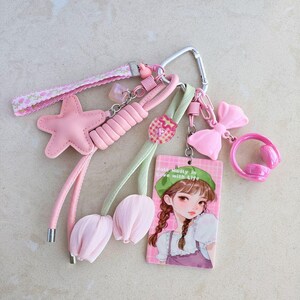 May include: A collection of pink keychains and charms, including a star, bow, and headphones. The keychains are attached to a silver carabiner. One charm features a cartoon girl with the text "Madly in love with life."
