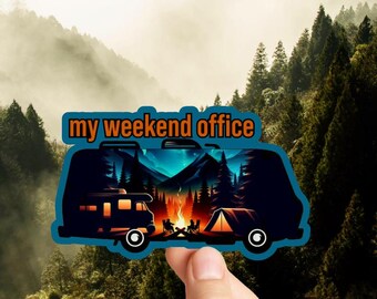 May include: A blue and orange sticker with a silhouette of a camper van in a forest setting. The text "my weekend office" is printed on the sticker.