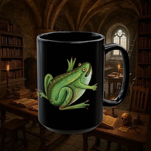 Puede incluir: Taza de cerámica negra con una ilustración de una rana verde. La rana tiene el vientre blanco y está sobre un fondo negro. La taza tiene un asa grande y es adecuada para bebidas frías o calientes.