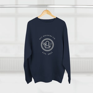 Könnte beinhalten: Ein marineblaues Sweatshirt mit einem weißen Logo, auf dem "Key Holders Co. Est. 2023" steht und ein Schlüsselloch mit gekreuzten Schlüsseln darin abgebildet ist.