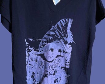 Puede incluir: Una camiseta con cuello en V de color azul marino oscuro con un gran diseño de mariposa en tonos morados. La mariposa está impresa sobre una forma rectangular texturizada. La camiseta tiene mangas cortas y una etiqueta en el cuello.