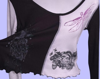 May include: A long-sleeved top with a V-neck design. The top is divided into two sections: black and off-white. The off-white section features a purple dragonfly and a black graphic print. The top has a ribbed texture and a scalloped hemline.